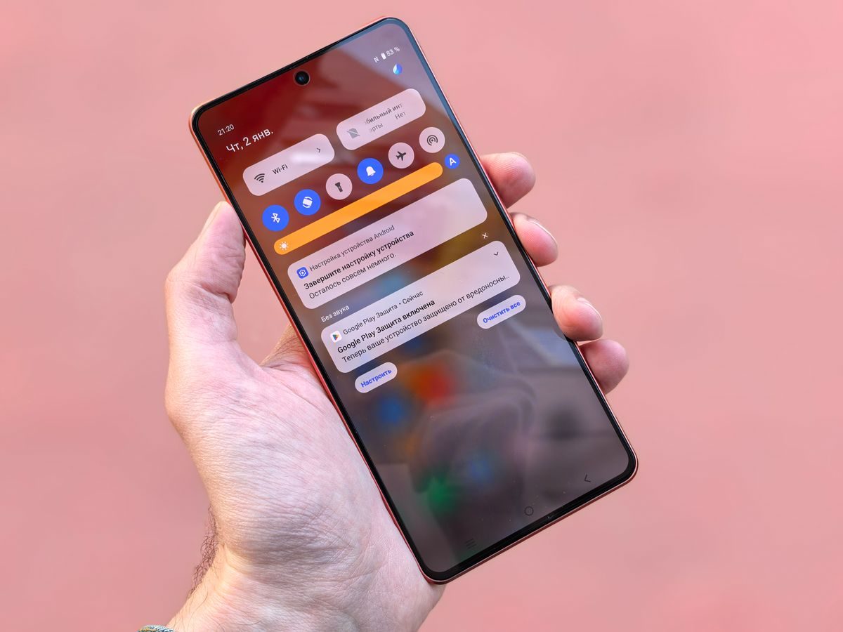 Hand holding an Android phone with the notification shade pulled down over Quick Settings
