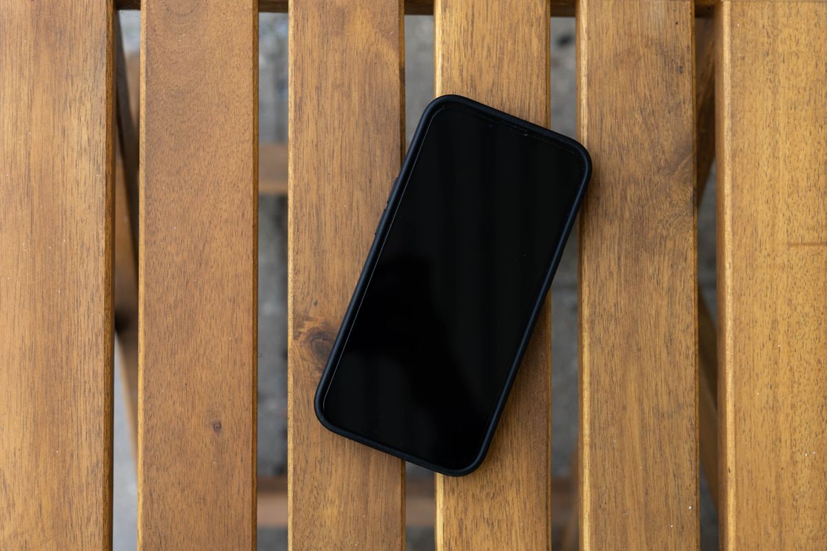 Smartphone with a dark screen lying on a wooden slatted table, viewed from above