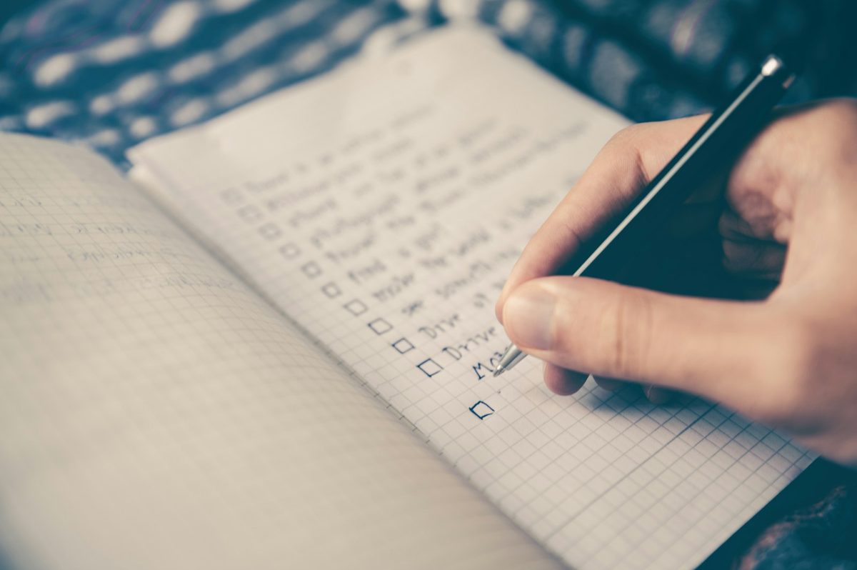 Hand writing a checklist with square checkboxes in a grid-paper notebook