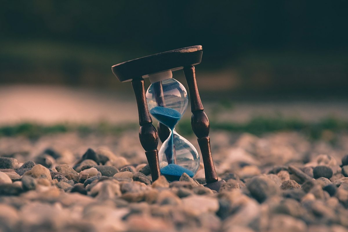 Wooden hourglass with blue sand flowing, resting on smooth river pebbles