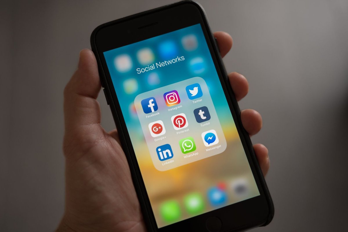 A hand holding a smartphone open to a folder of social media apps