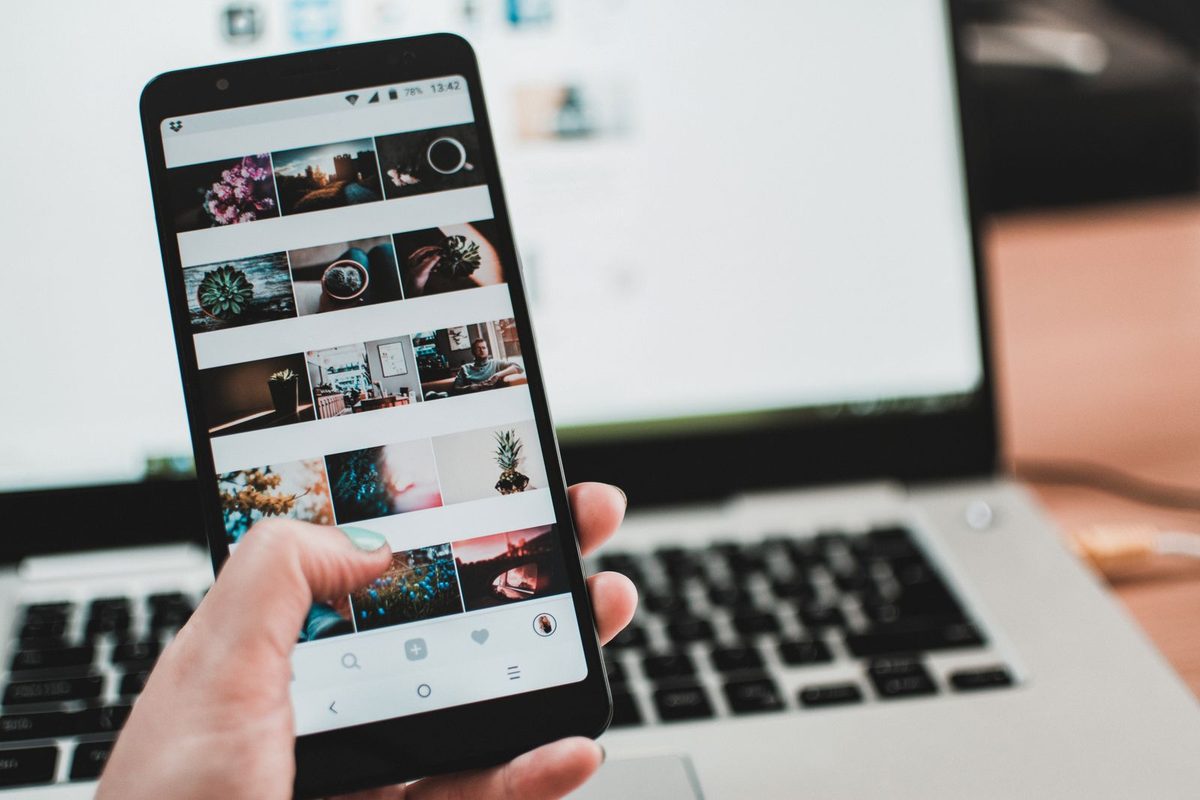 Hand holding an Android phone showing a social feed in front of an open laptop