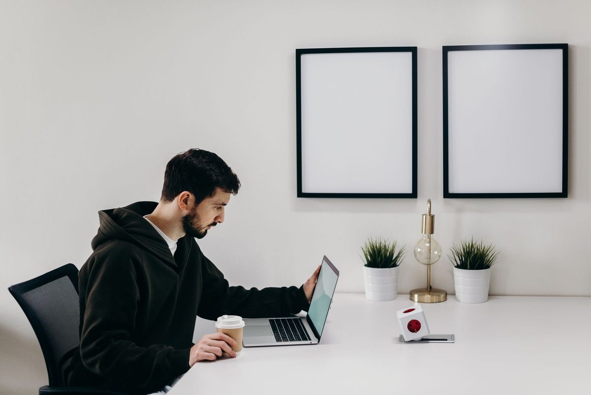 Person at a minimalist white desk with a laptop, coffee cup, lamp, and small plants