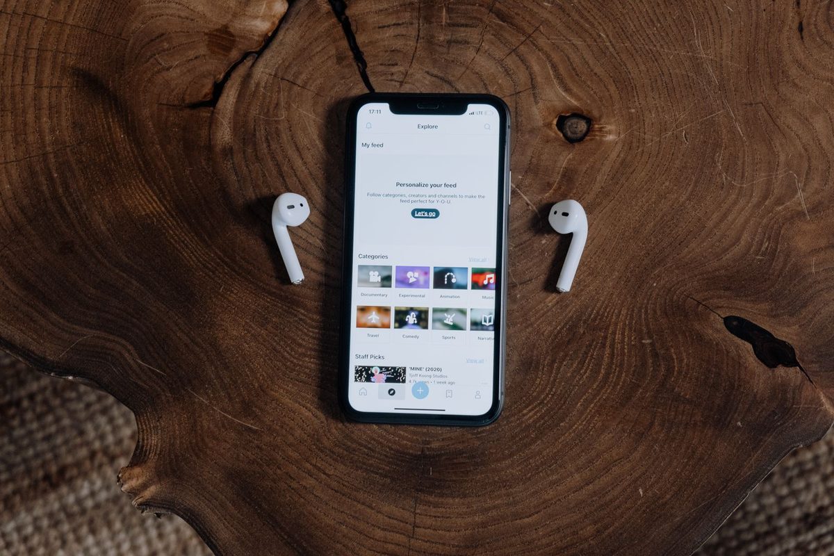 Black smartphone and white wireless earbuds resting on a dark wooden table