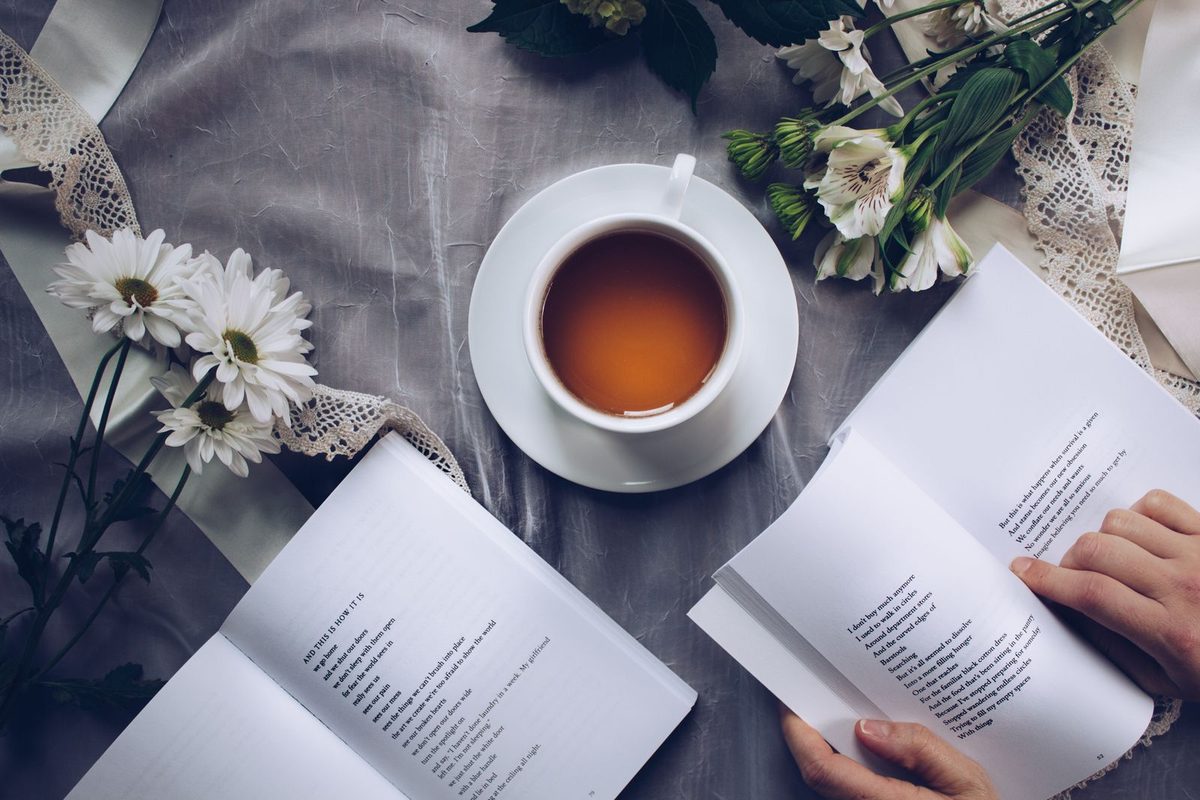 Cup of tea, open books, and white flowers arranged on a gray cloth for a screen-free break