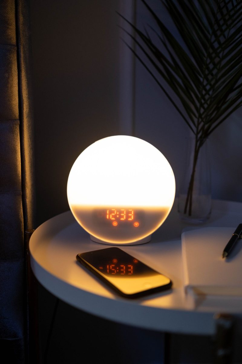 Phone lying on a small round side table at night next to a glowing round alarm clock