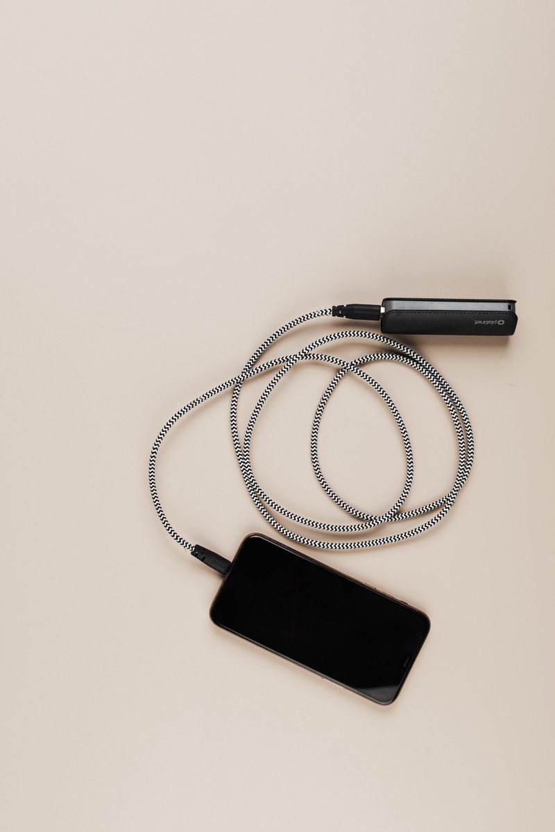 Smartphone lying face up on a light surface, charging from a small power bank through a coiled gray cable
