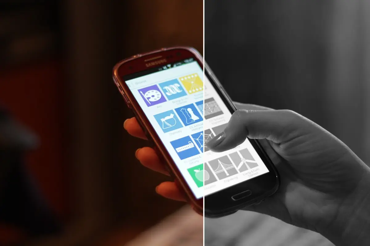 A hand holding an Android phone with a grid of colorful app tiles, the left side of the photo in full color and the right side in grayscale