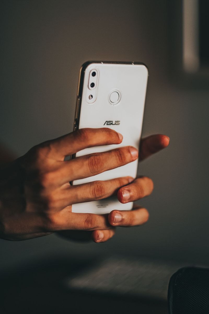 Two hands holding a white smartphone with its back toward the camera in a dim room