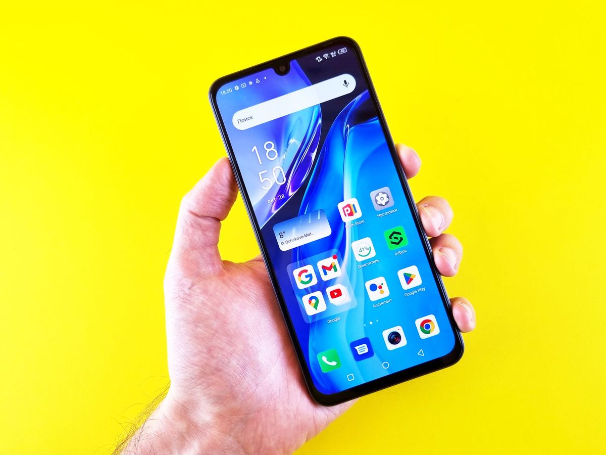 Hand holding an Android phone with a home screen of app icons against a bright yellow background