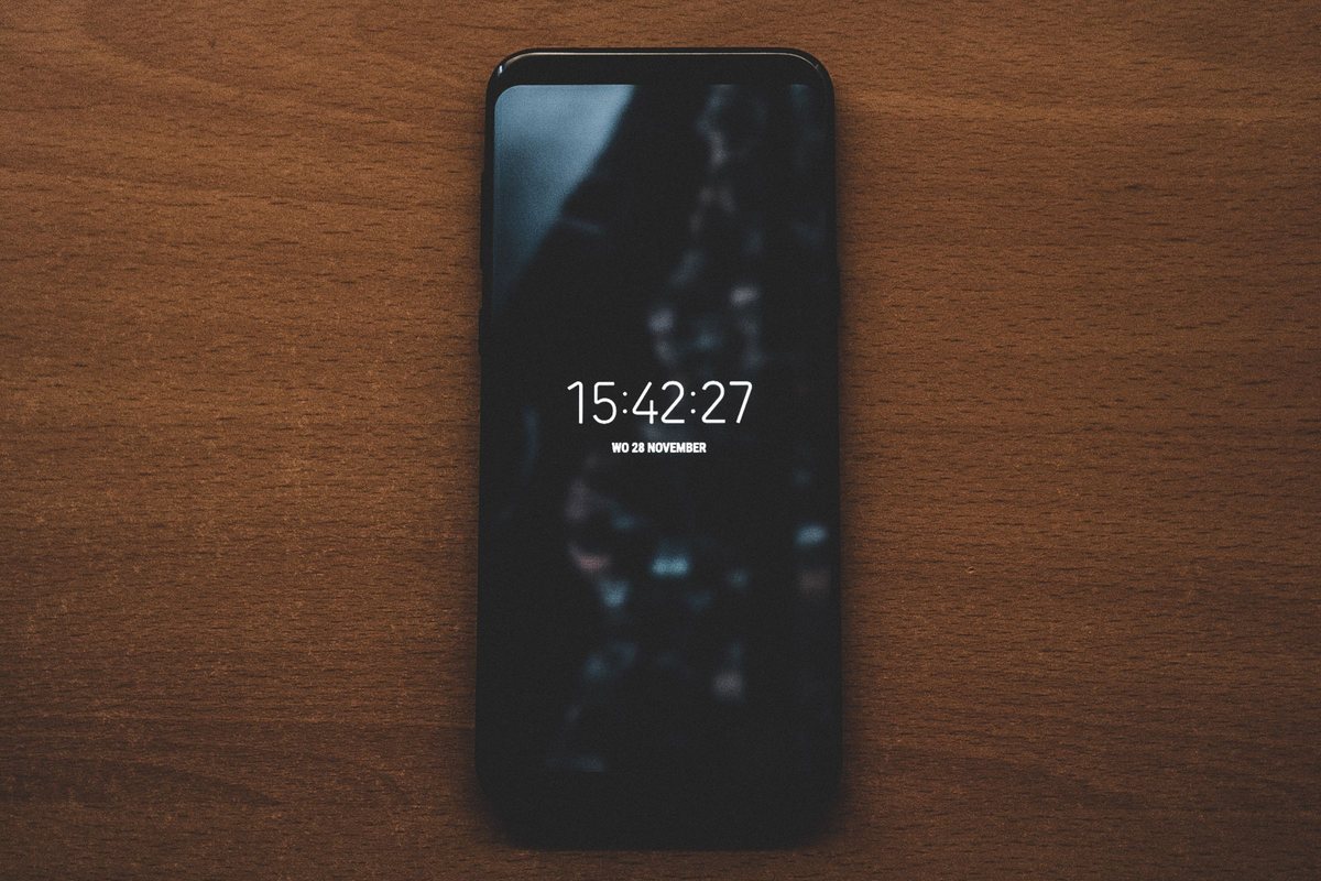 A black smartphone lying on a wooden table with its lock screen showing only the time and date
