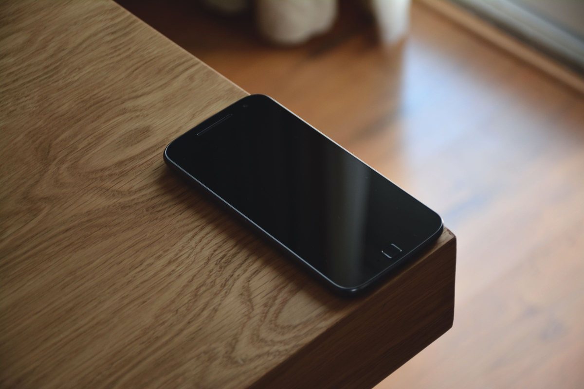 A black smartphone with a dark screen lying on the corner of a wooden table