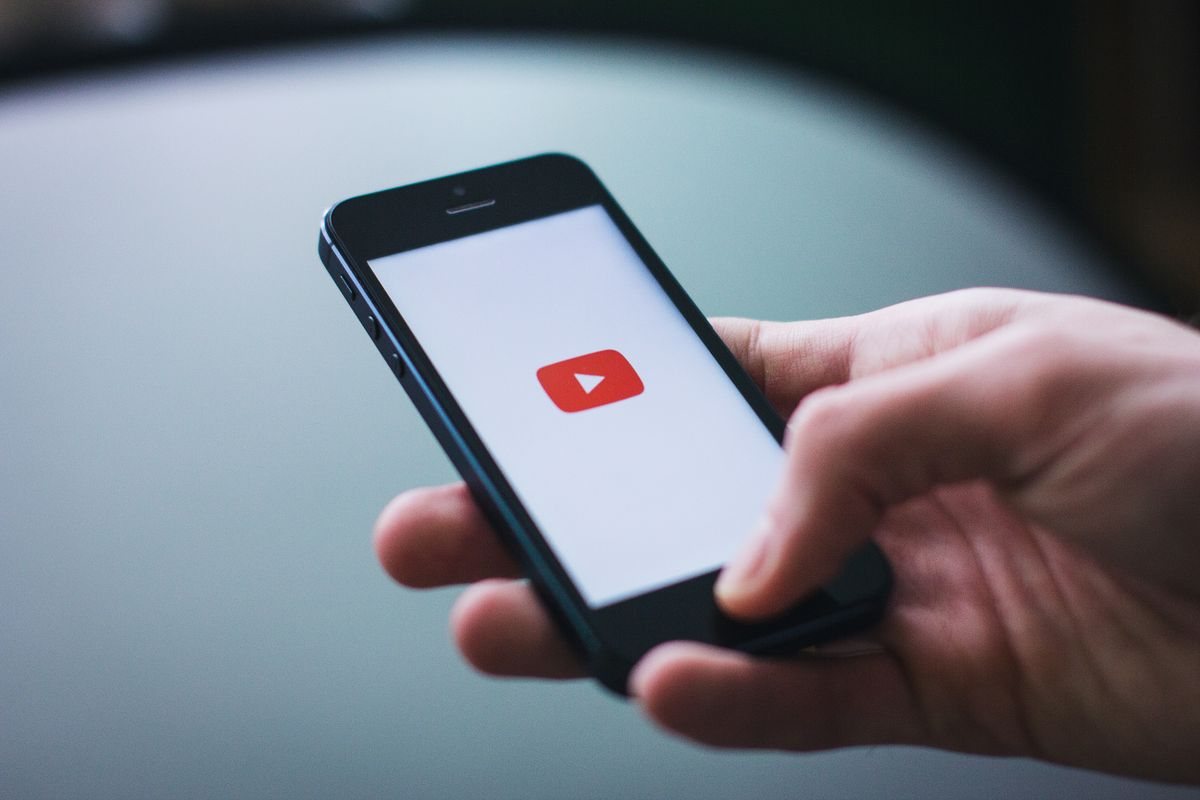 A hand holding a smartphone with the YouTube logo on the screen
