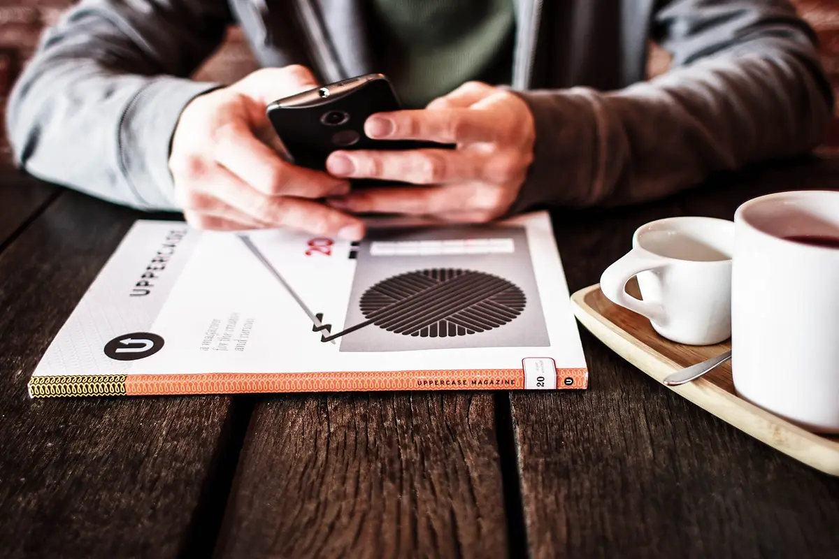 A smartphone lying on a wooden table next to a cup of coffee