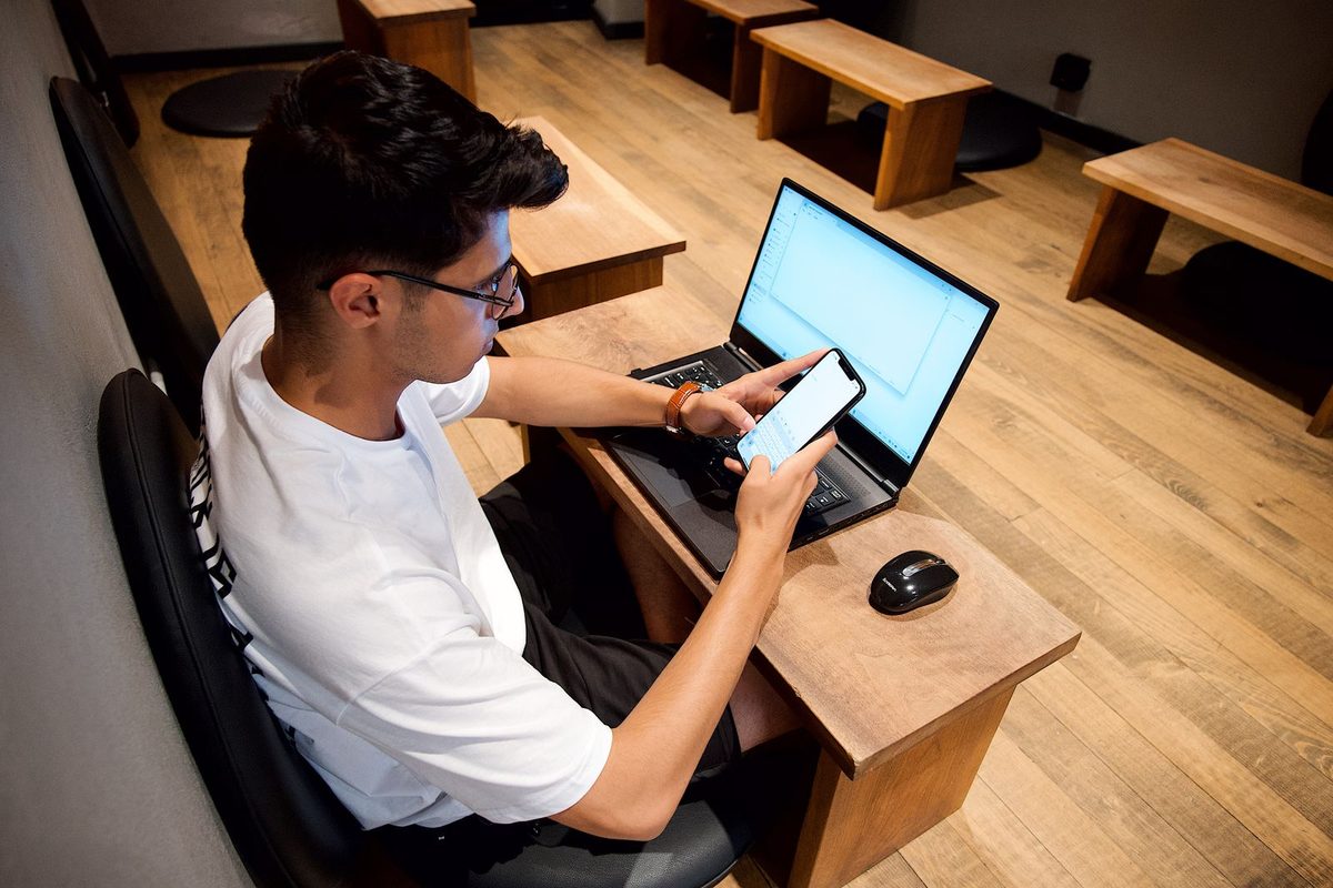 Man sitting at a desk using a smartphone with a laptop open beside him