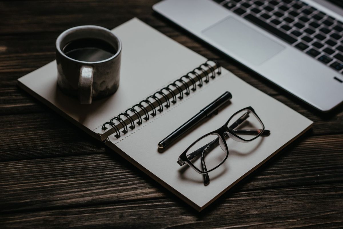 Open notebook with a cup of coffee and eyeglasses resting on a desk