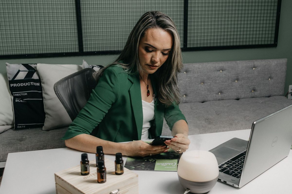 Businesswoman at a desk checking her smartphone while a laptop sits open in front of her