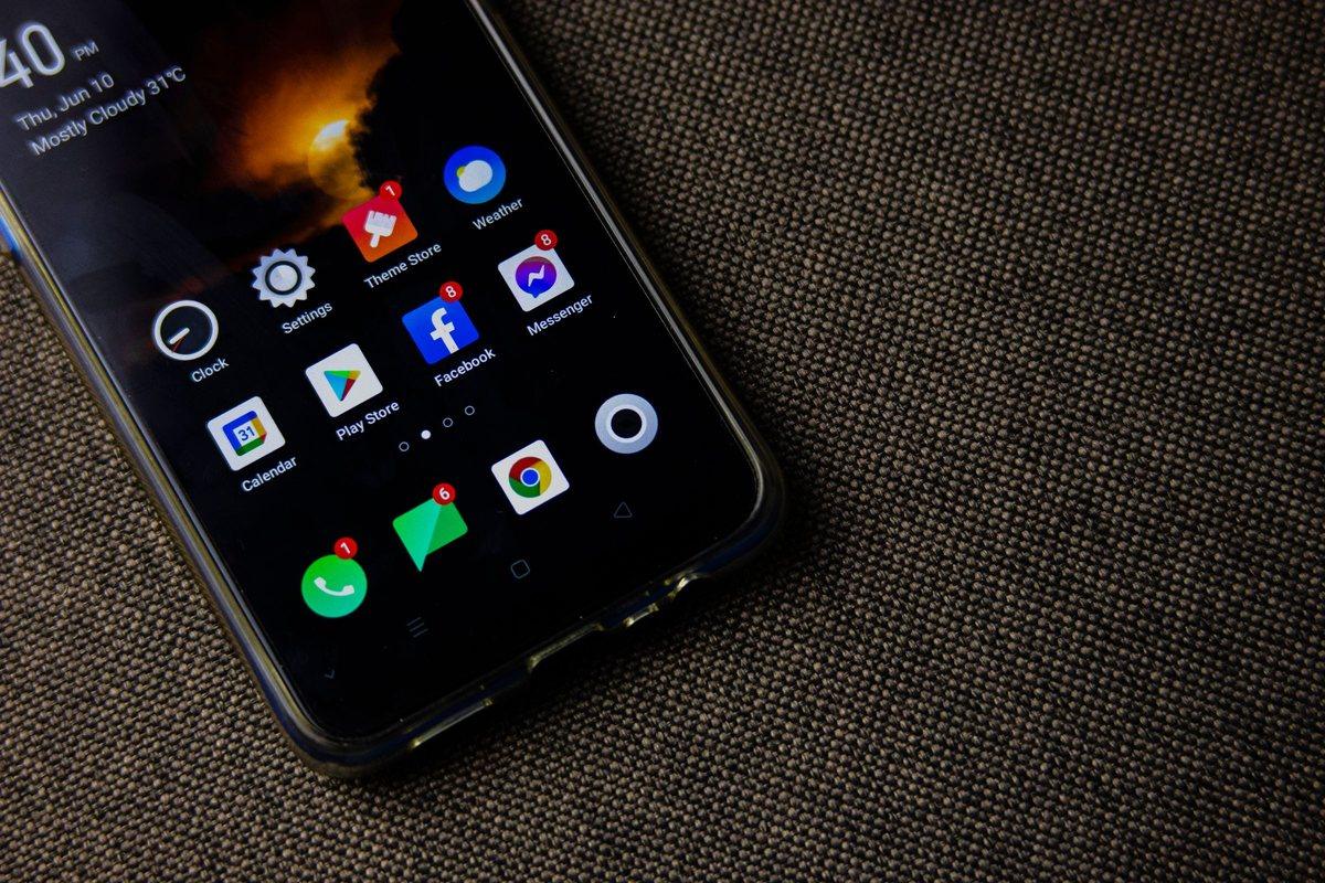 An Android phone on a grey fabric surface, its home screen showing red number badges on the Facebook, Messenger, Phone, Messages, and Theme Store icons