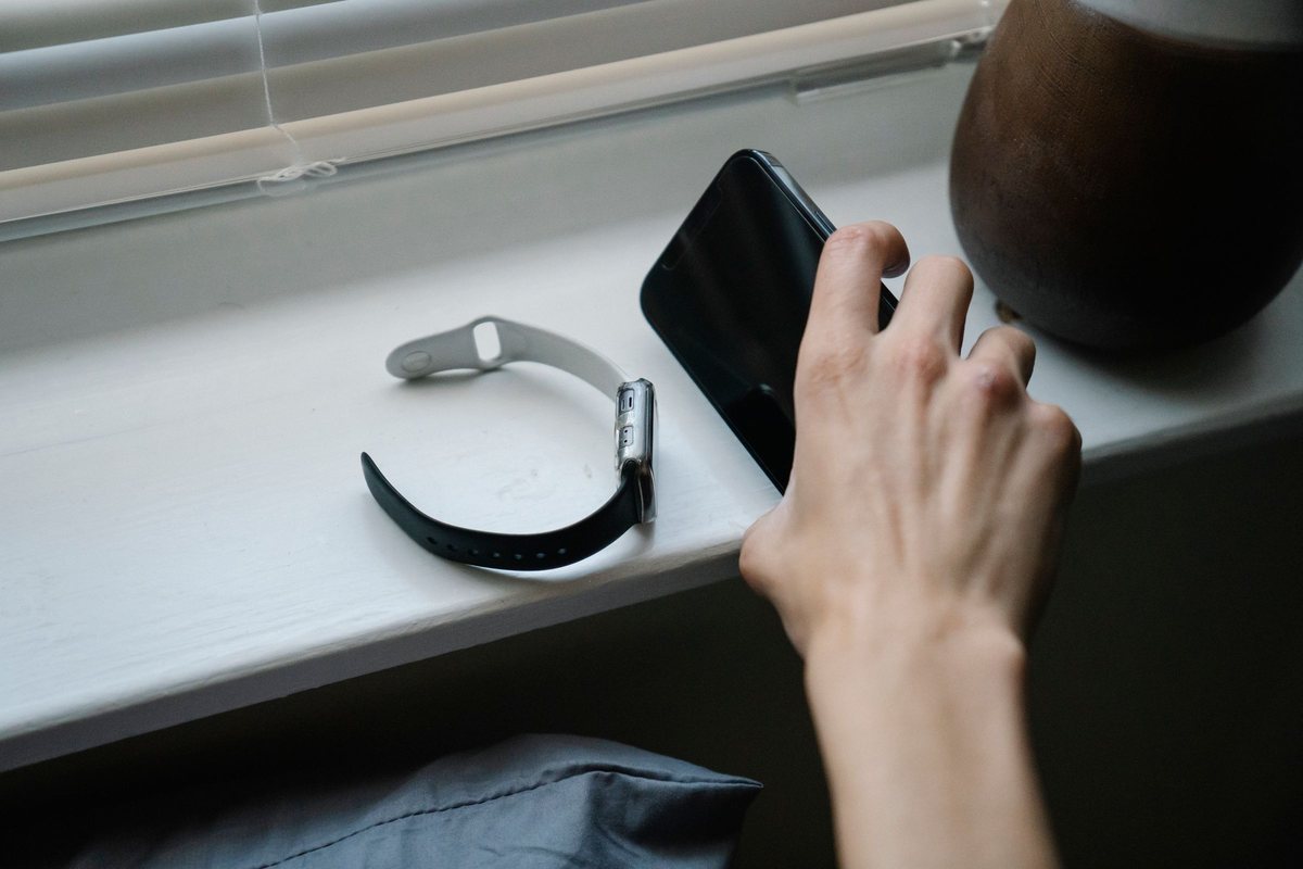 A hand reaching for a phone lying on a white windowsill next to a smartwatch with its strap open