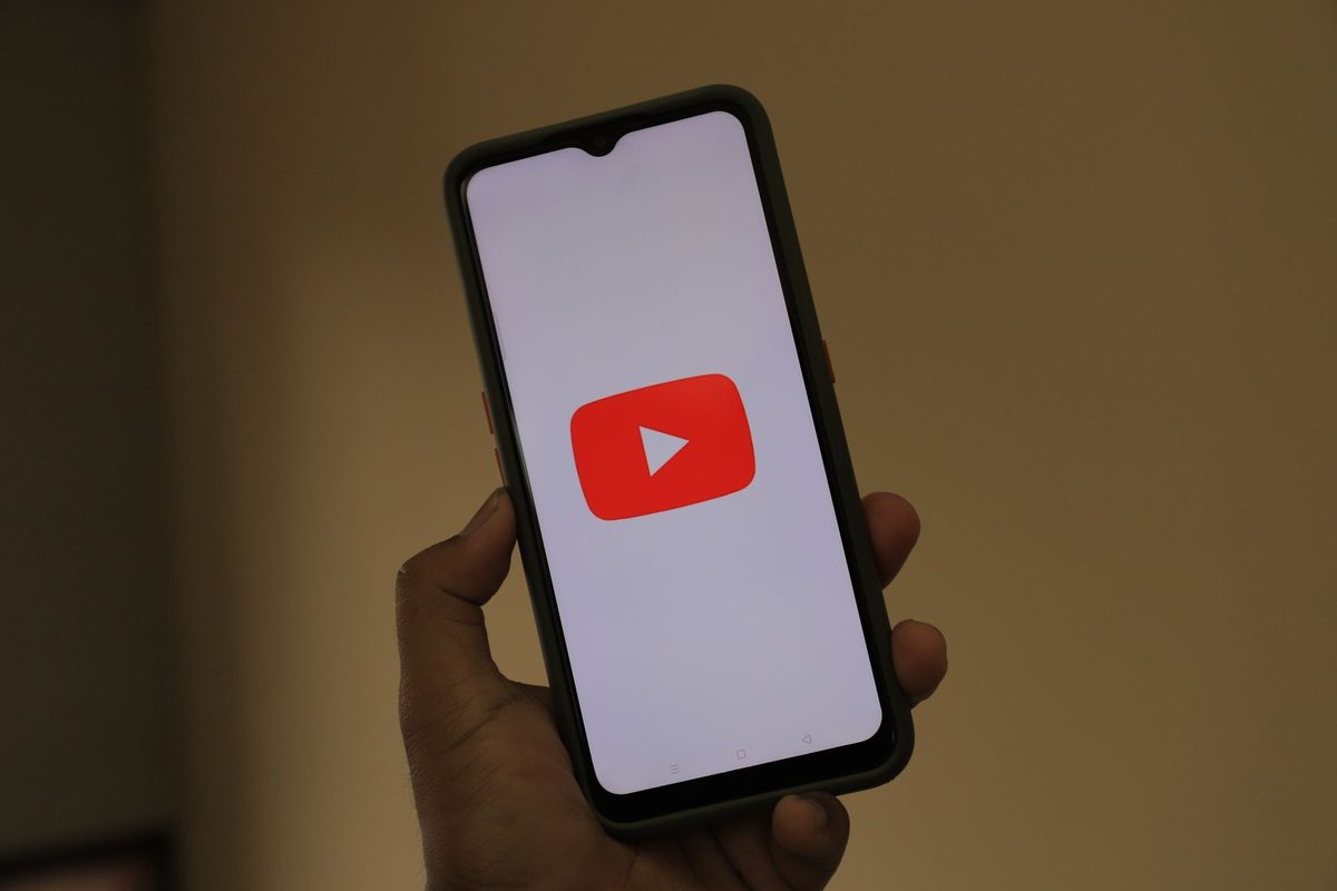 A hand holding an Android phone showing the YouTube logo on a white screen in a dim room