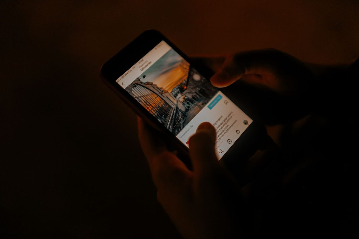 Hands holding a smartphone in a dark room, the screen lighting up the fingers