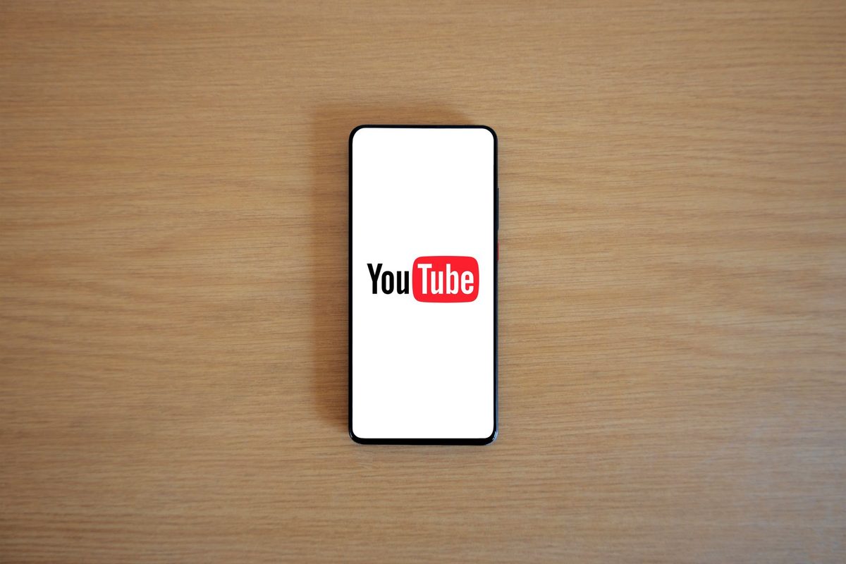 A smartphone lying on a wooden table with the YouTube logo on its screen